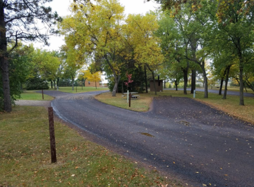 A winding road through a park with trees displaying autumn colors and a signpost in the foreground.