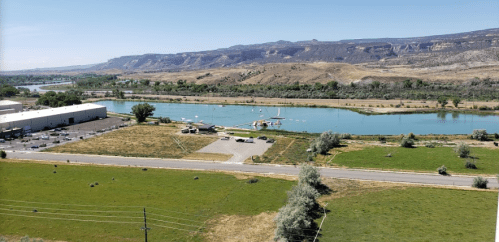 A scenic view of a river surrounded by hills, with a parking area and green fields in the foreground.