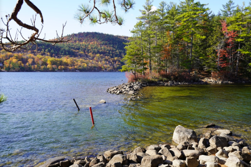 A serene lake scene with colorful autumn trees, rocky shorelines, and clear water under a bright blue sky.