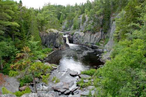 A serene landscape featuring a waterfall cascading into a river, surrounded by lush greenery and rocky cliffs.