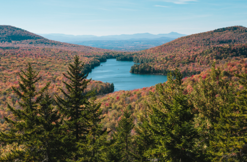 A scenic view of a lake surrounded by vibrant autumn foliage and mountains under a clear blue sky.