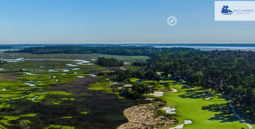 Aerial view of a lush golf course surrounded by marshland and water, under a clear blue sky.