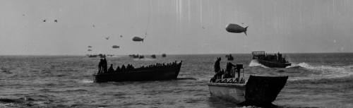 Black and white image of boats on water, with airships above and people onboard, creating a historical maritime scene.