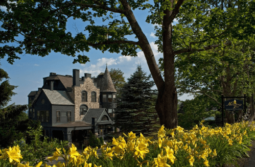 A historic mansion surrounded by lush greenery and vibrant yellow flowers under a clear blue sky.