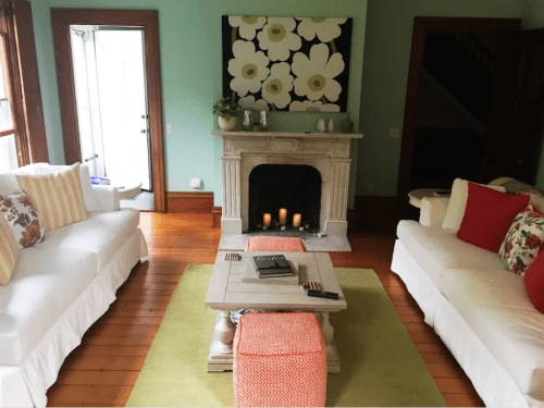 Cozy living room with white sofas, a stone fireplace, a coffee table, and floral artwork on the wall.