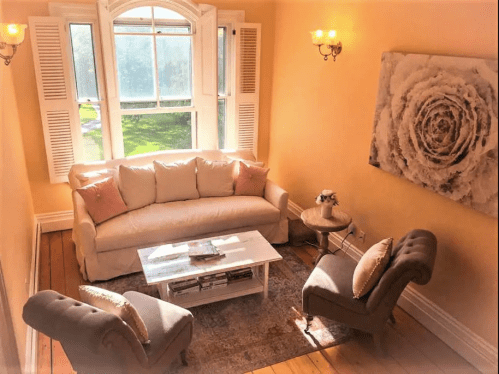 Cozy living room with a light sofa, armchairs, a coffee table, and large windows letting in natural light.
