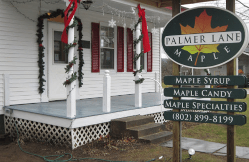 A white house with red shutters, decorated for the holidays, featuring a sign for Palmer Lane Maple and its products.