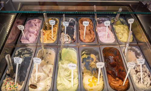 A display of various gelato flavors in metal containers, each labeled with a name, showcasing colorful, creamy textures.