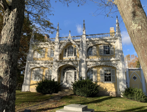 A yellow Gothic-style house with ornate details, surrounded by trees and a clear blue sky.