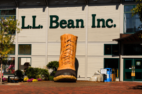 A giant boot sculpture stands outside the L.L. Bean Inc. store, surrounded by colorful flowers and a clear blue sky.