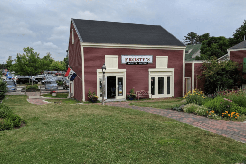 A red building with a sign reading "Frosty's Donuts & Coffee," surrounded by greenery and a parking lot in the background.