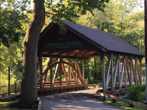 A wooden covered bridge at Lincoln Woods State Park, surrounded by lush greenery and trees.