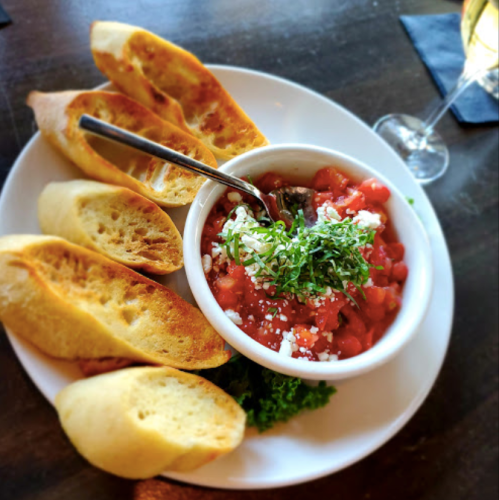 A plate of toasted bread slices served with a bowl of tomato salad topped with herbs and feta cheese.