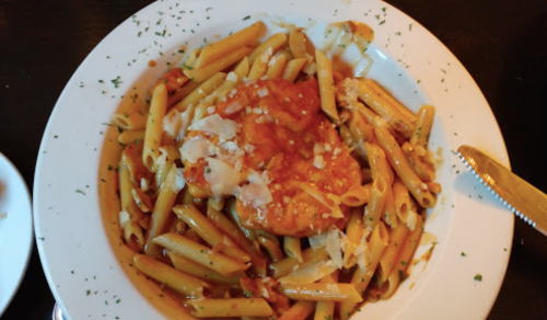 A plate of penne pasta topped with marinara sauce and a breaded chicken cutlet, garnished with cheese and herbs.