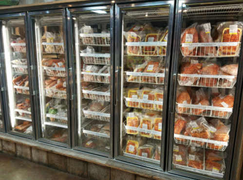 A display of frozen meat packages in a grocery store freezer, organized in clear bins.
