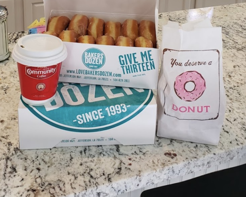 A box of donuts, a coffee cup, and a paper bag with a donut graphic on a kitchen countertop.