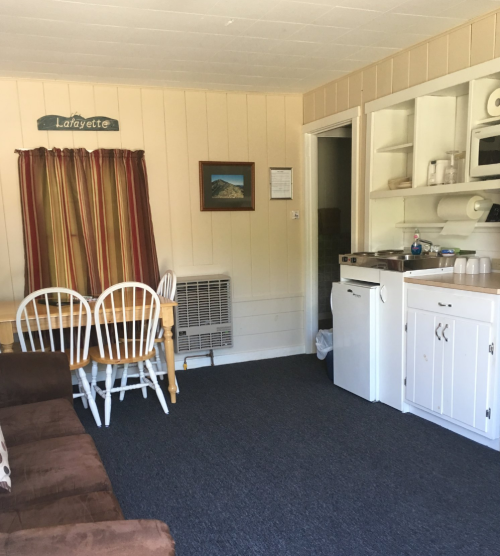 Cozy room with a dining table, chairs, kitchenette, and air conditioning unit, featuring warm-colored curtains.