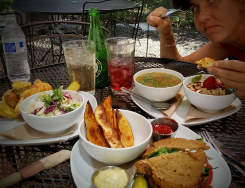 A table set with various dishes, including salad, soup, fries, and a sandwich, with a person eating in the background.