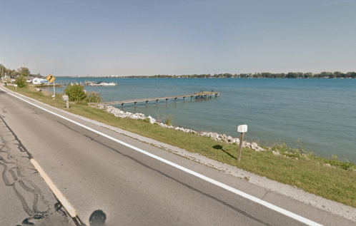A calm waterfront scene featuring a dock, boats, and a road alongside a serene body of water.