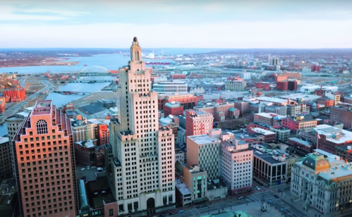 Aerial view of a city skyline with tall buildings, waterfront, and a clear sky in the background.