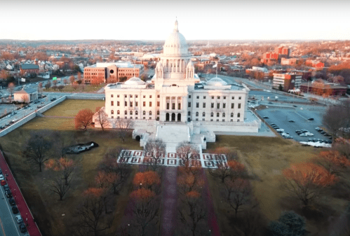 Aerial view of a grand government building with a dome, surrounded by trees and cityscape in the background.