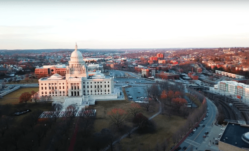 Aerial view of a large government building with a dome, surrounded by cityscape and trees during sunset.