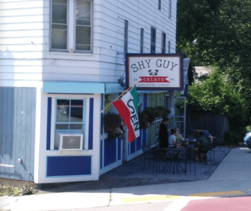 Exterior of Shy Guy Gelato shop with an "OPEN" flag and people sitting outside in a sunny setting.