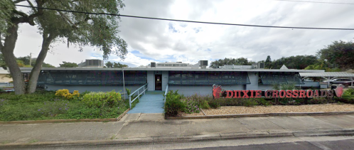 Exterior view of Dixie Crossroads restaurant, featuring a blue entrance and landscaping under a cloudy sky.
