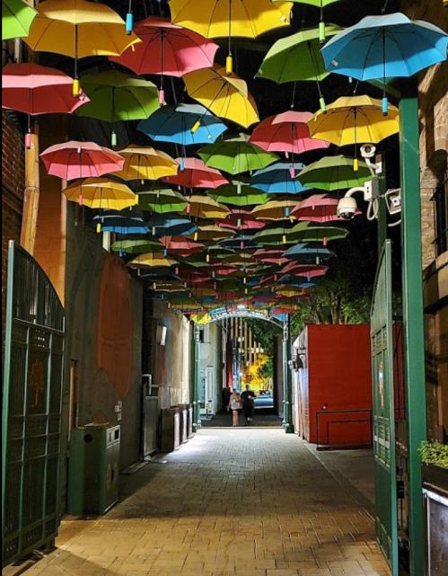 A vibrant alleyway at night adorned with colorful hanging umbrellas, creating a whimsical atmosphere.