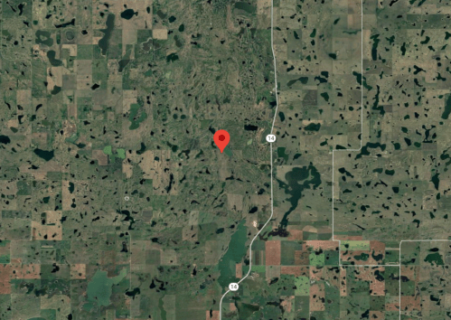 Aerial view of a rural landscape with fields, lakes, and a red location marker.