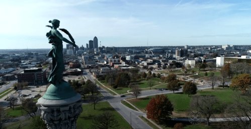 Aerial view of a city skyline with a statue in the foreground, surrounded by parks and autumn foliage.