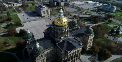 Aerial view of a grand building with a golden dome, surrounded by green spaces and empty parking lots.