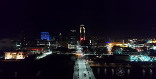 Aerial view of a city skyline at night, featuring illuminated buildings and a busy road.