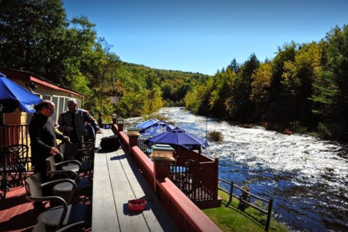 A scenic view of a river surrounded by trees, with a deck and umbrellas in the foreground.