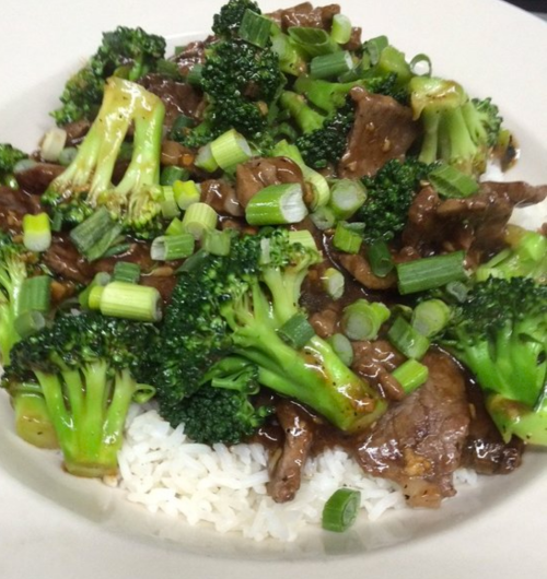 A plate of beef and broccoli stir-fry served over white rice, garnished with green onions.