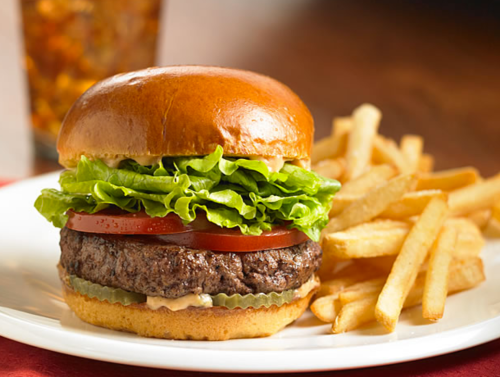 A juicy hamburger with lettuce, tomato, and pickles, served with a side of golden fries on a white plate.
