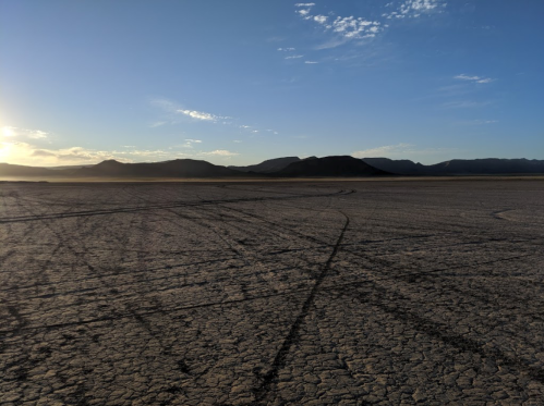 A vast, dry landscape with cracked earth and distant mountains under a clear blue sky at sunset.