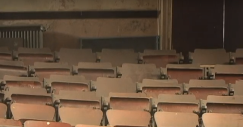Empty, worn-out auditorium seats with a dusty atmosphere and a partially visible radiator in the background.