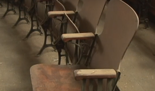 Abandoned wooden chairs with metal frames in a dusty, empty room.