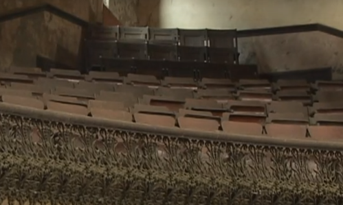 Abandoned theater seating with ornate detailing, showcasing empty wooden chairs and a faded, worn interior.