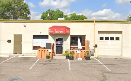 Exterior of a small eatery with a red awning, potted plants, and a garage door, set in a parking lot.