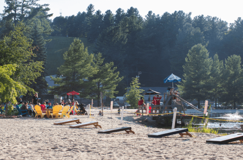 A sandy beach scene with colorful chairs, people enjoying the sun, and a lifeguard station by the water.