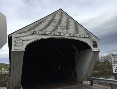 A covered bridge with a sign that reads, "Walk your horses or pay two dollars five." Overcast sky in the background.