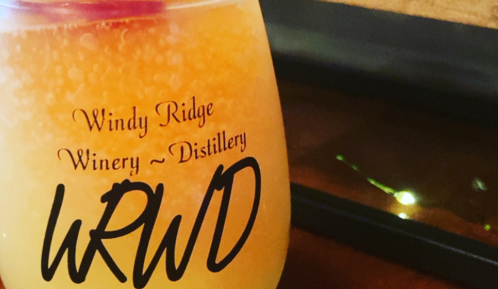 A close-up of a colorful drink in a glass with "Windy Ridge Winery ~ Distillery" printed on it.