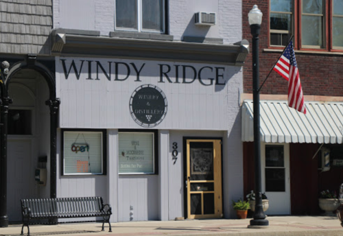 Exterior of Windy Ridge Distillery with an American flag, a bench, and a sign indicating it's open.