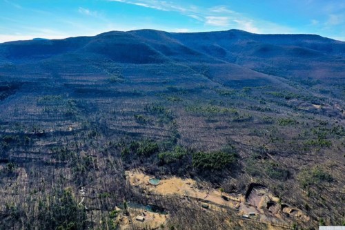Aerial view of a mountainous landscape with sparse vegetation and a clear blue sky.