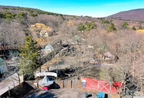 Aerial view of a rural area with bare trees, old buildings, and a sign for Crystal Lake Farm in the foreground.