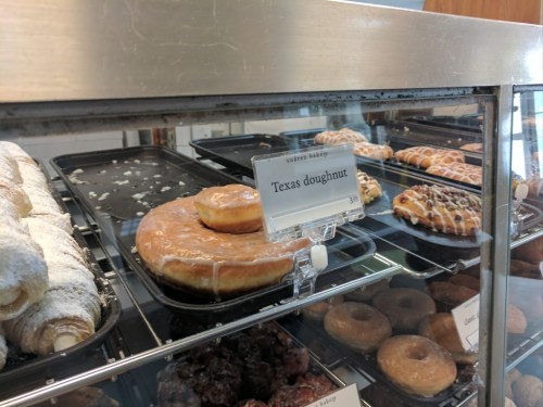 Display case of assorted doughnuts, featuring a Texas doughnut with a glaze and various other pastries.
