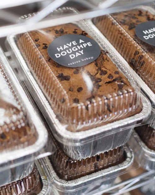 Loaves of chocolate chip dough in clear packaging, labeled "Have a Doughpe Day" from a bakery.