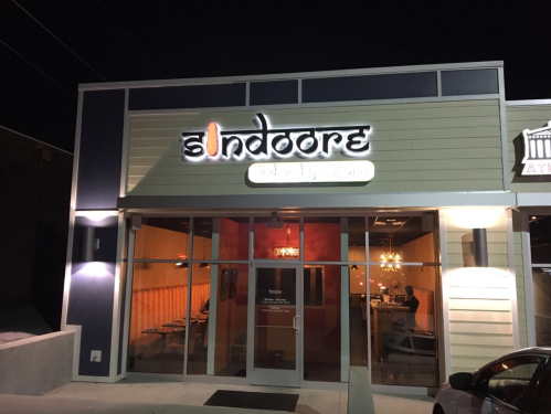 Exterior of a restaurant named "Sindoore," illuminated at night with a modern design and warm interior lighting visible.